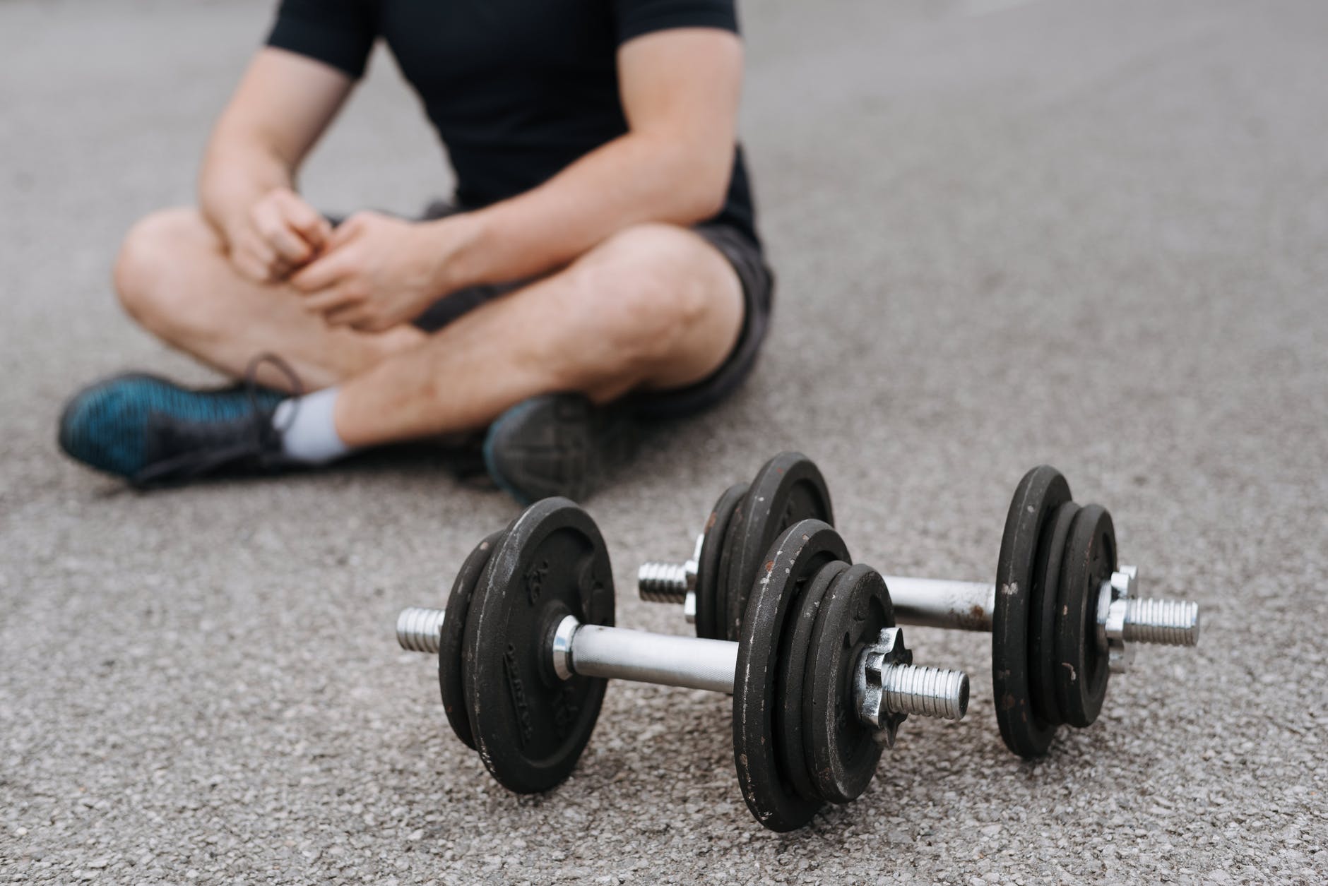 man with dumbbells in lotus pose on asphalt road